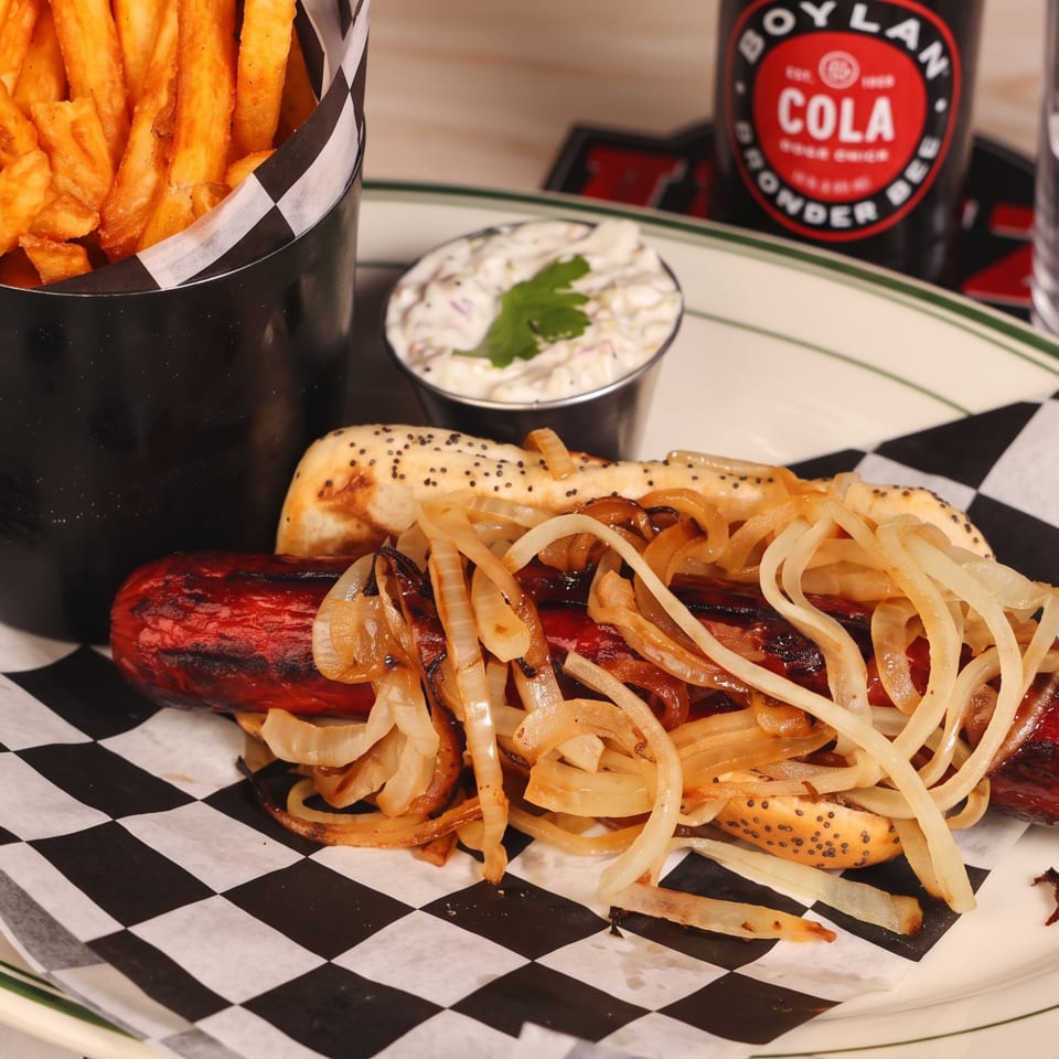 Grilled sausage topped with onions in a poppy-seed bun, served with fries, creamy coleslaw, and Boylan cola.