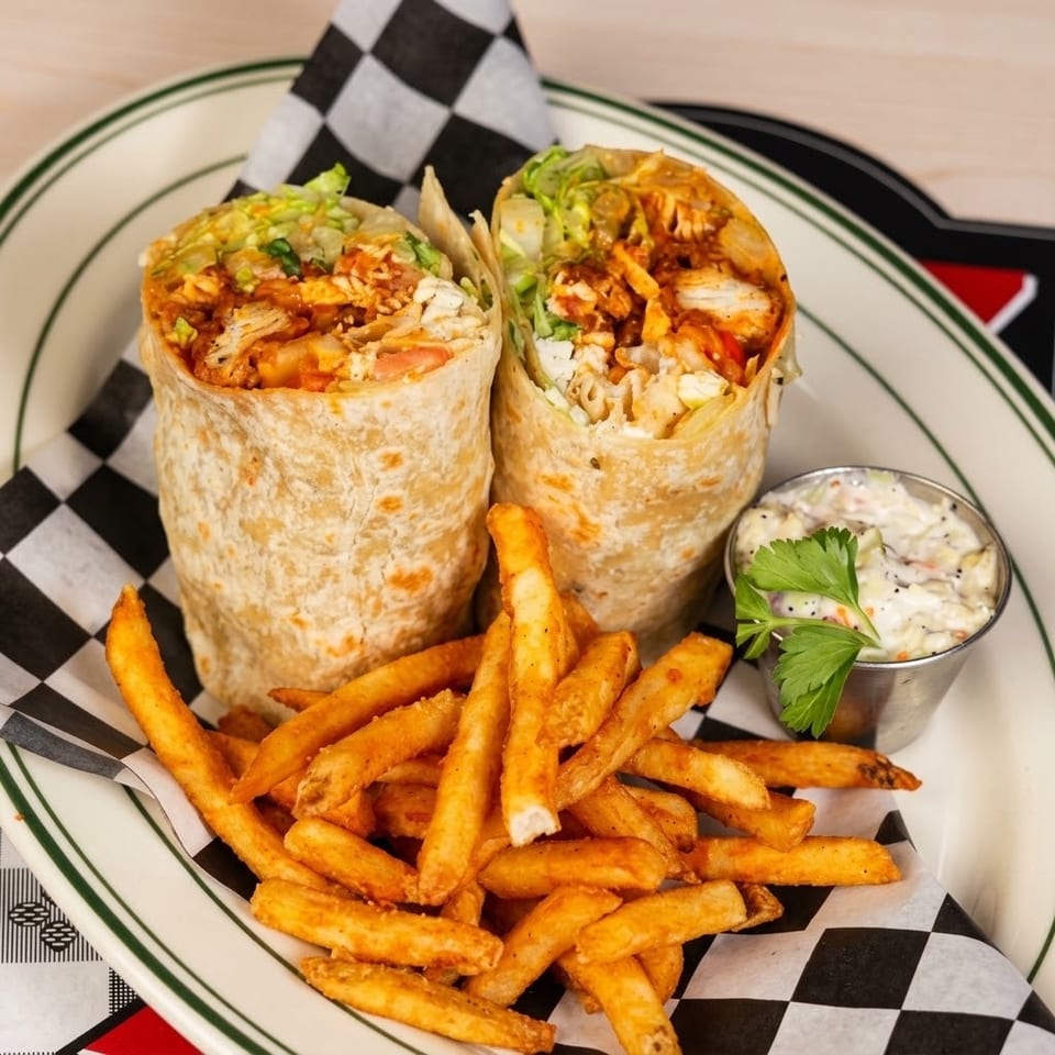Grilled chicken burrito halves with lettuce and sauce, served alongside seasoned fries and creamy dipping sauce on a diner plate.